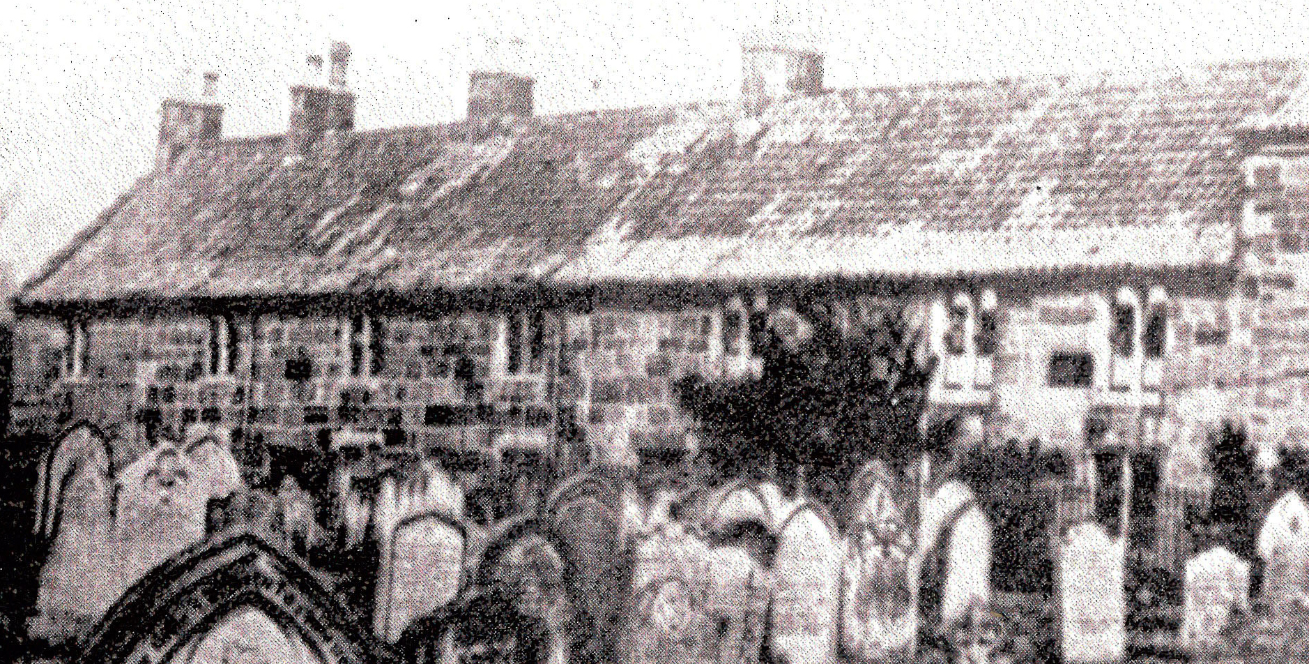 A row of small sandstone houses with a tiled roof and chineys, seen over a graveyard. The photographs is in sepia and was taken c.1860.