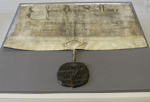 Parchment document with black writing, very faded. It has a green wax seal at the bottom suspended on a length of cord. 