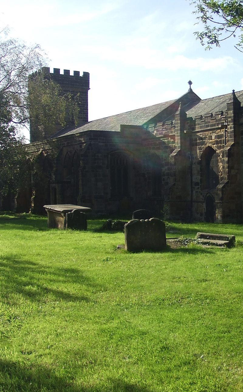 Colour photograph of a medieval church in a churchyard with gravestones.