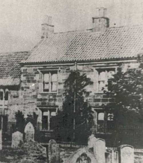 An old photograph of a building which housed the free grammar school in Guisborough until the 1880s. In the foreground are gravestones, as the photograph was taken from St Nicholas' Church yard. 