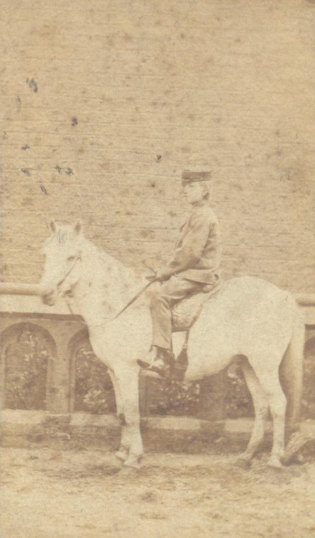 A sepia photo from the 1860s of a schoolboy sitting on a pony in front of a wall. 