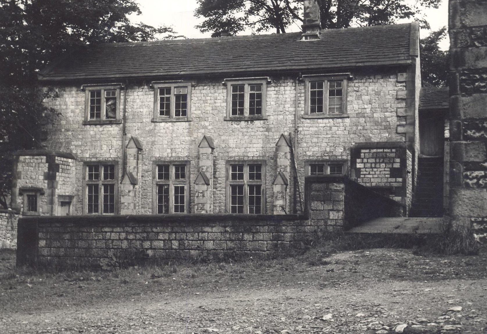 Black and white photograph of the Old Grammar School Tideswell, a two storey stone building with square-headed windows. 